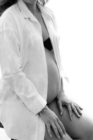 Black and white maternity photo showing a pregnant belly with woman wearing an open white button-down shirt.