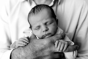A peaceful sleeping newborn baby rests against an adult's forearm in black and white.