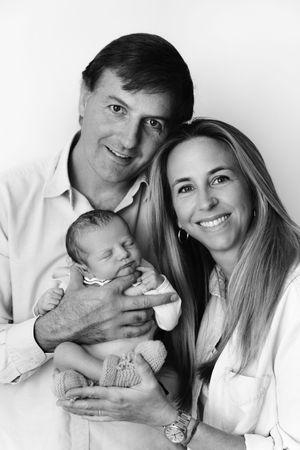 Black and white studio portrait of three people with a newborn baby, captured in a warm and intimate family setting.