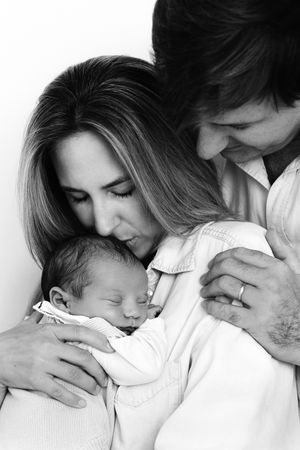Intimate black and white family portrait showing loving parents cradling their sleeping newborn baby.
