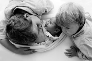 A tender black and white moment between a parent and small child resting together on white bedding.
