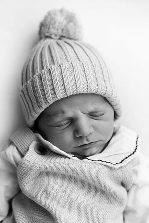 Sweet sleeping newborn baby wearing a cozy white knit hat with pom pom and matching sweater in black and white photo.