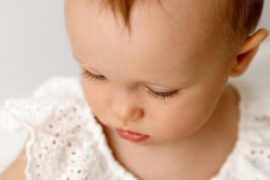 A young child wearing a white lace dress looks downward in a soft portrait closeup.