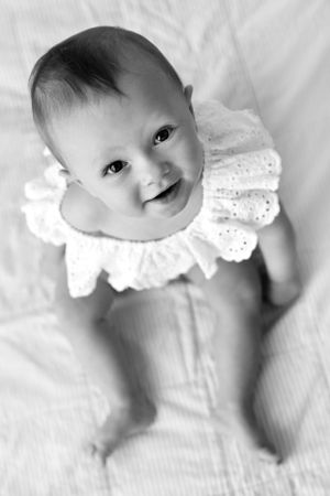 Black and white photo of a smiling baby in an eyelet lace collar lying on white fabric.