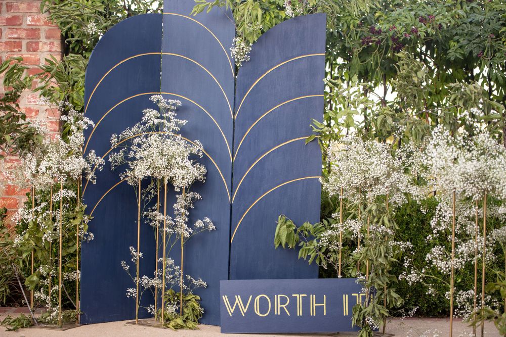 Navy blue decorative arch with 'WORTH IT' text against brick wall with white flowers.