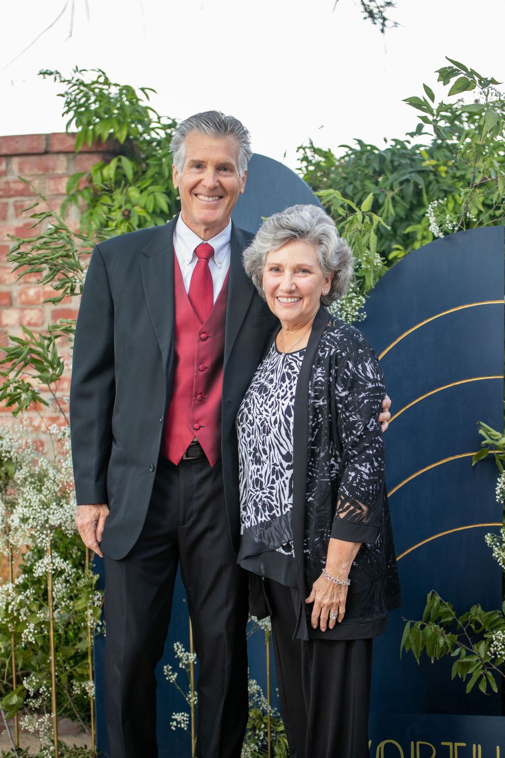 Formal portrait taken in front of a decorative navy blue backdrop with foliage.