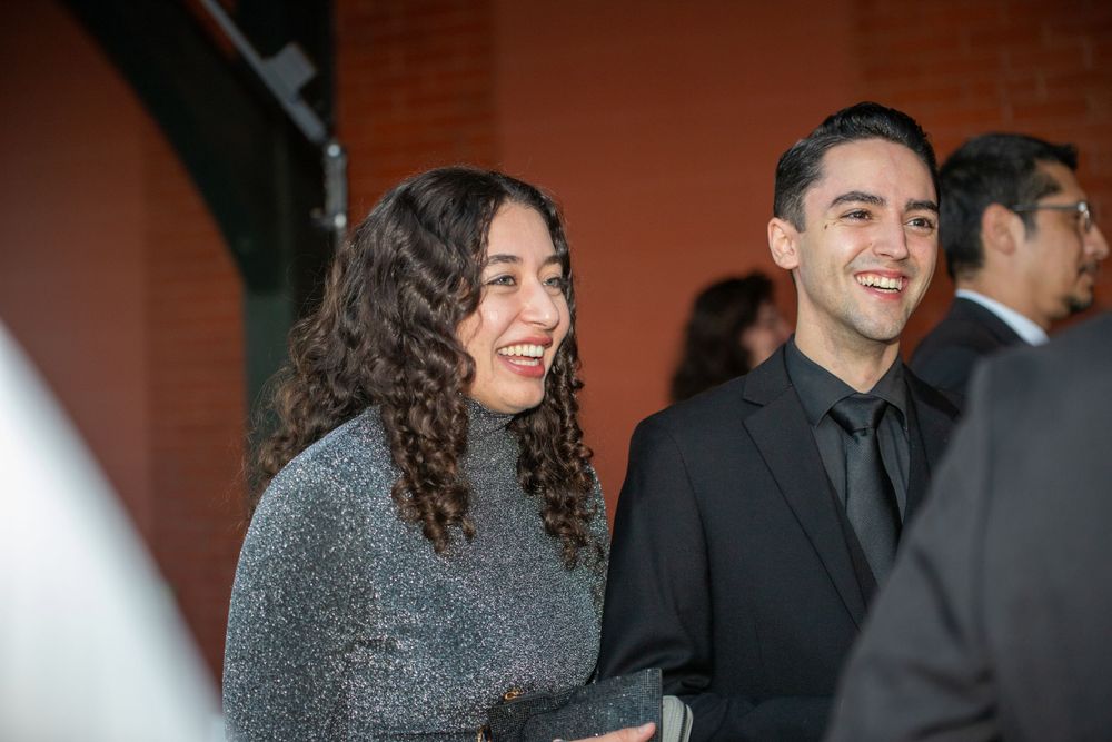 Attendees engaged in lively conversation at an elegant evening banquet with golden chairs and warm lighting.