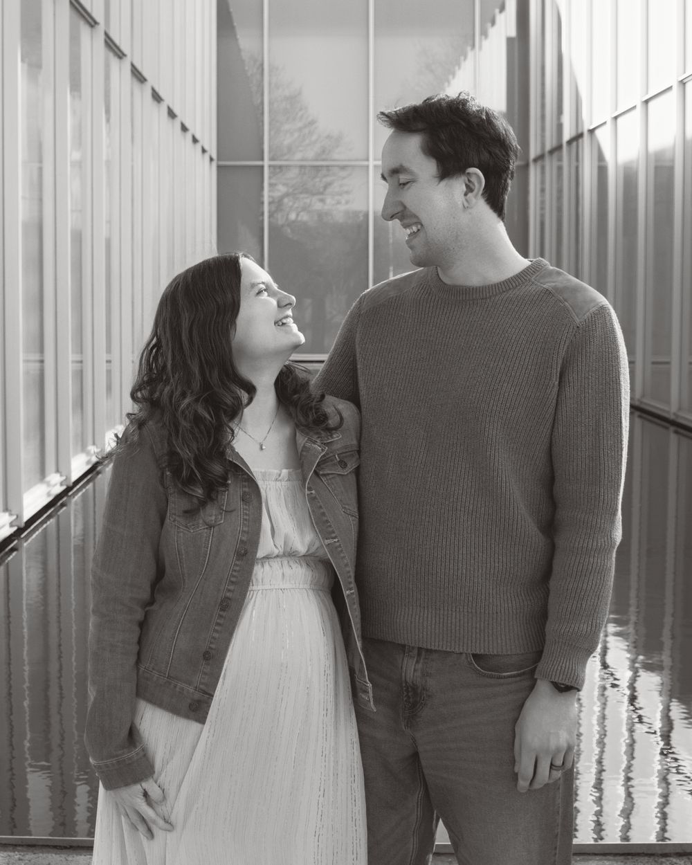 A couple shares a joyful moment together in a hallway, captured in black and white photography.