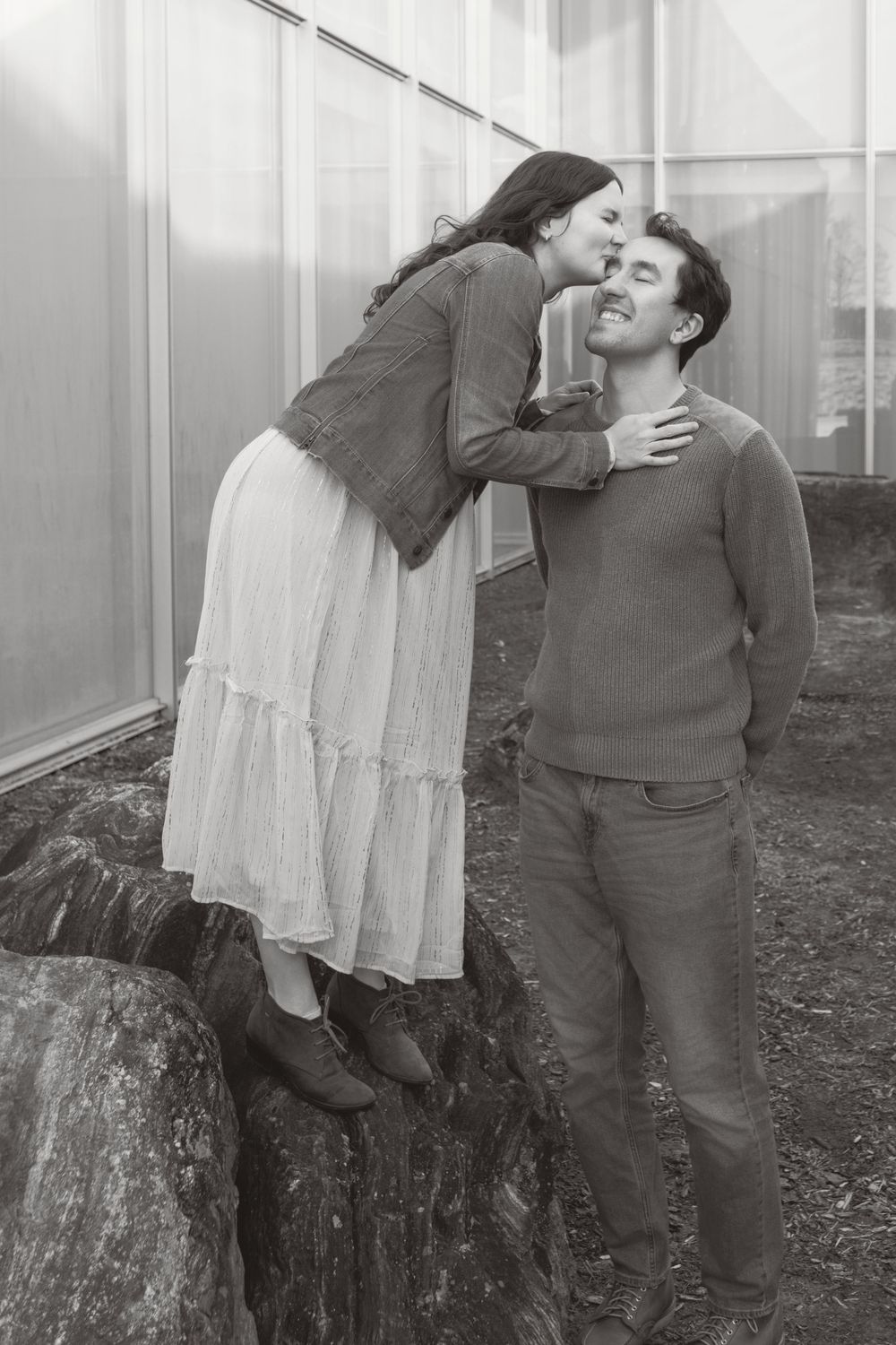 Black and white romantic photo showing couple sharing a tender moment outdoors near a stone wall.