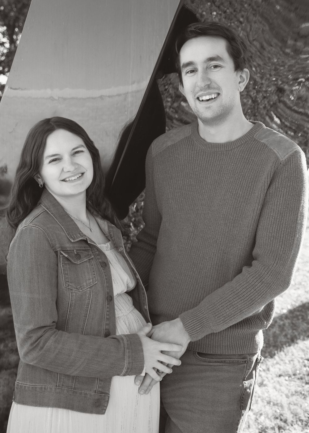 A black and white portrait of a happy couple smiling while standing together outdoors in casual attire.