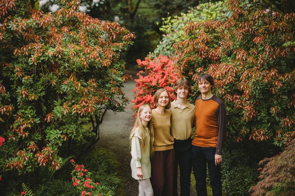 Family stand together on Bellevue botanical garden path surrounded by vibrant spring foliage and red flowering bushes.