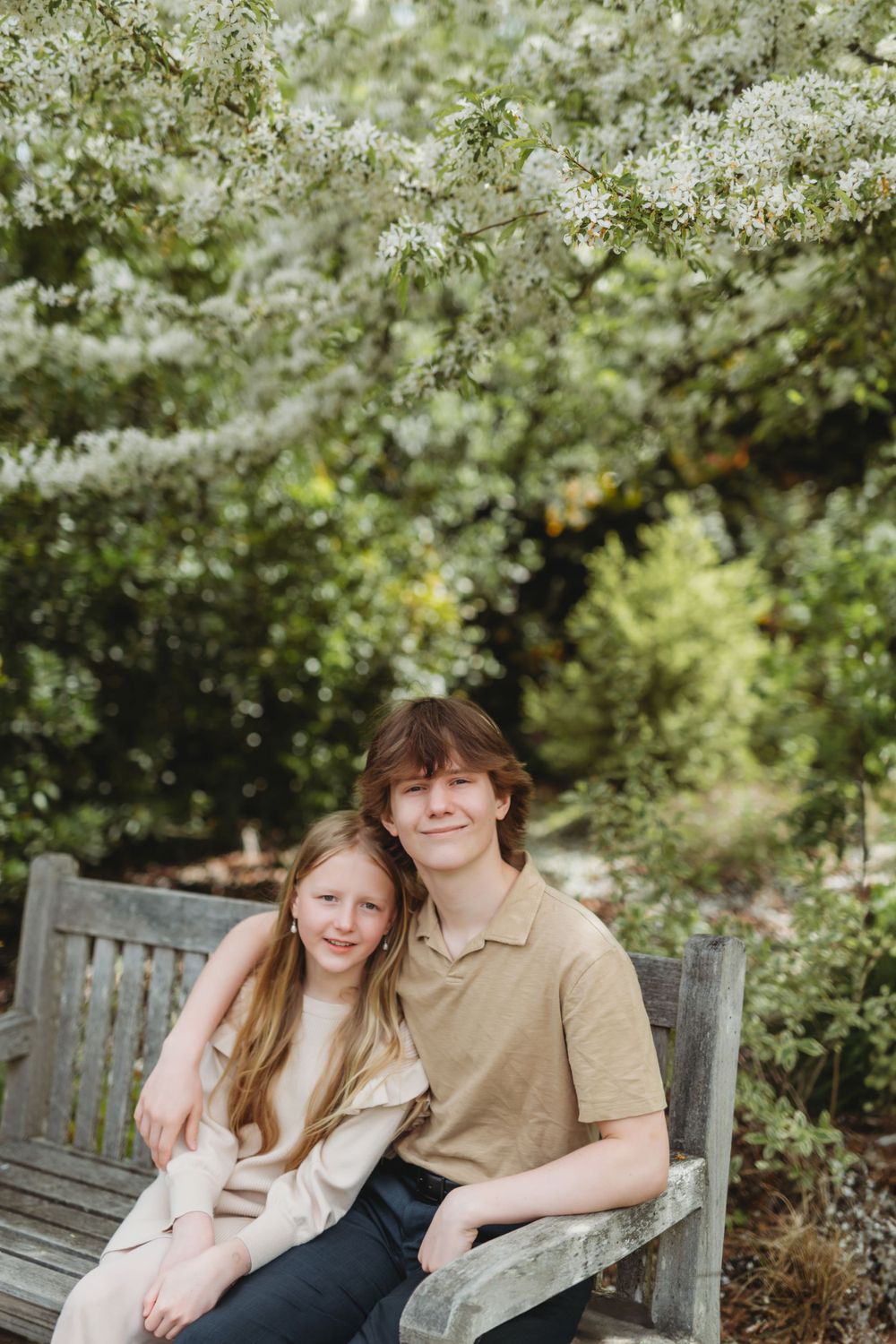 Two people sit close together on a wooden bench under blooming spring trees in Bellevue botanical  garden setting.