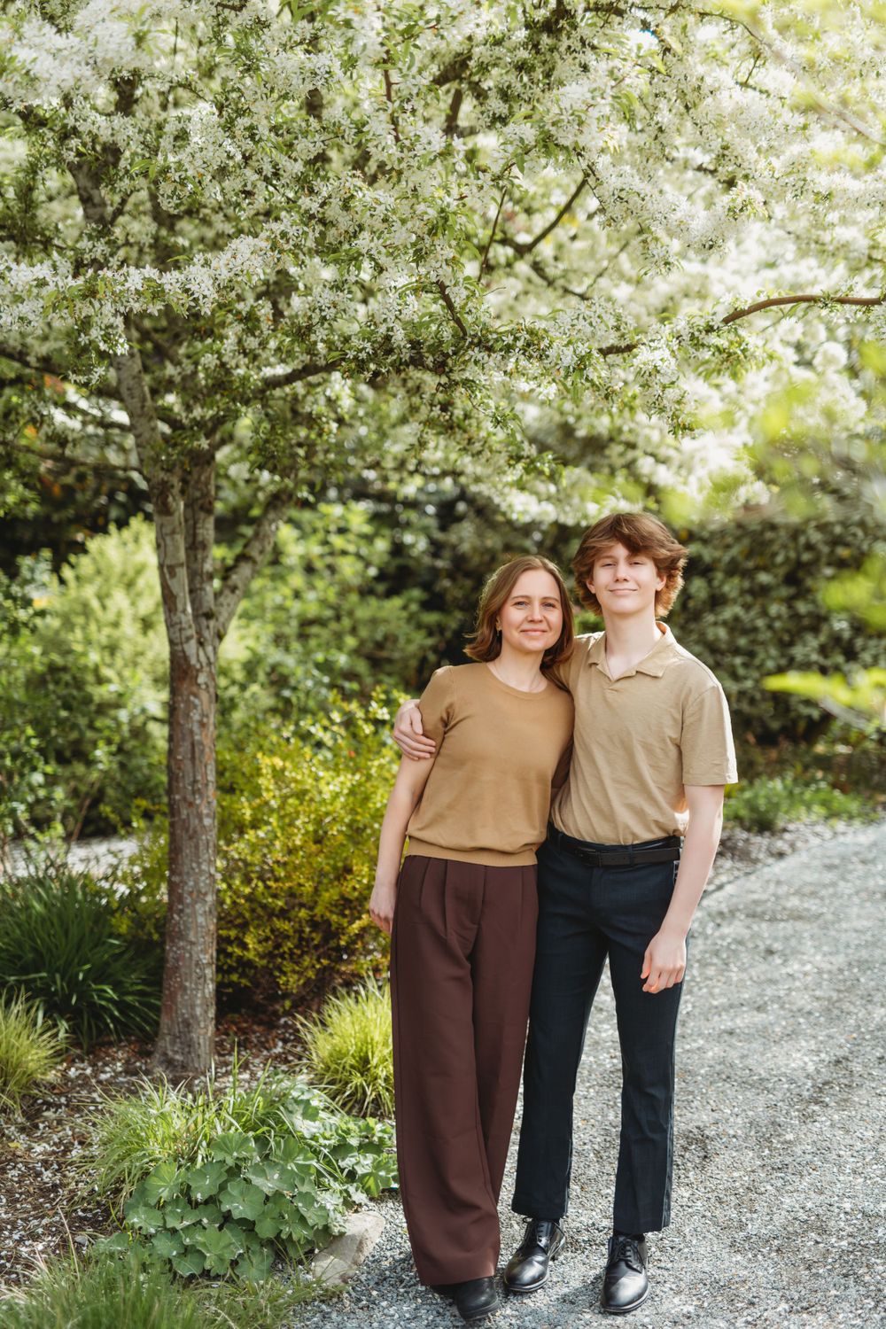 Mom and son stand together on a garden path under blooming white spring blossoms on a sunny day Bellevue botanical  garden.