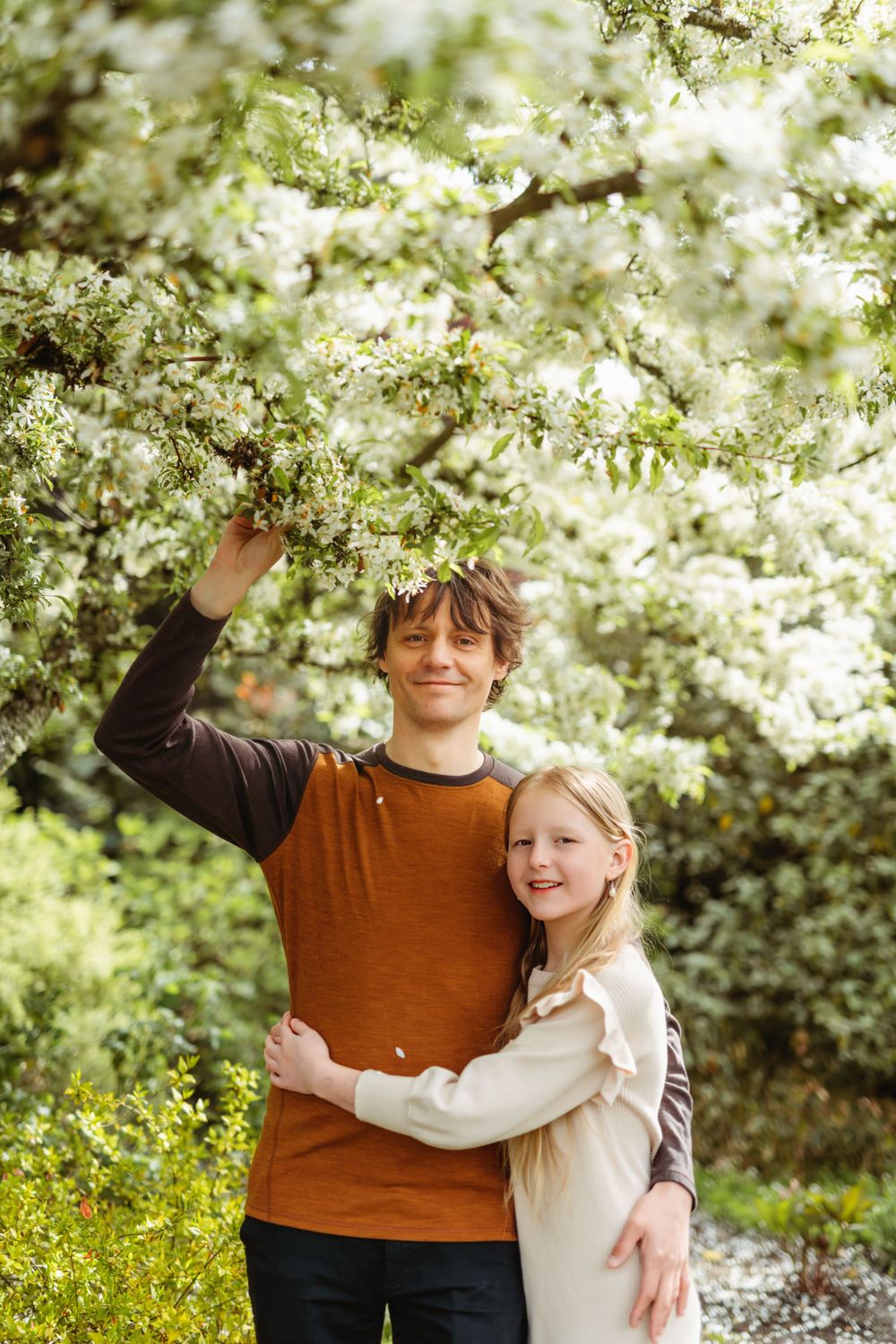 Dad and daughter smiling under blooming white cherry blossoms on a bright spring day in Bellevue botanical garden.