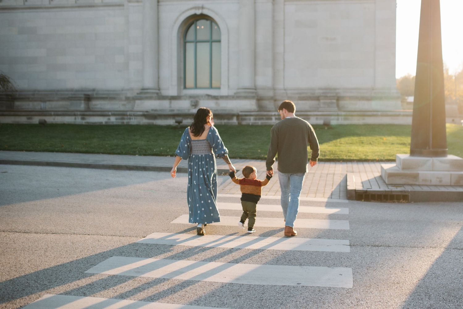 Family holds hands while crossing pedestrian walkway at golden hour.