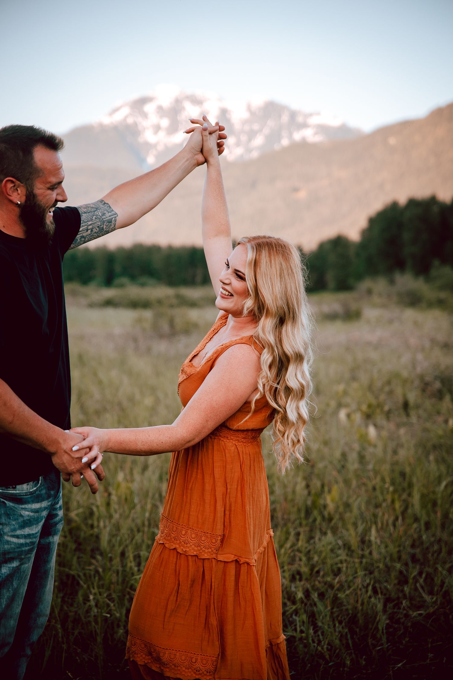 Couple dancing together in a field with mountains in background at golden hour.