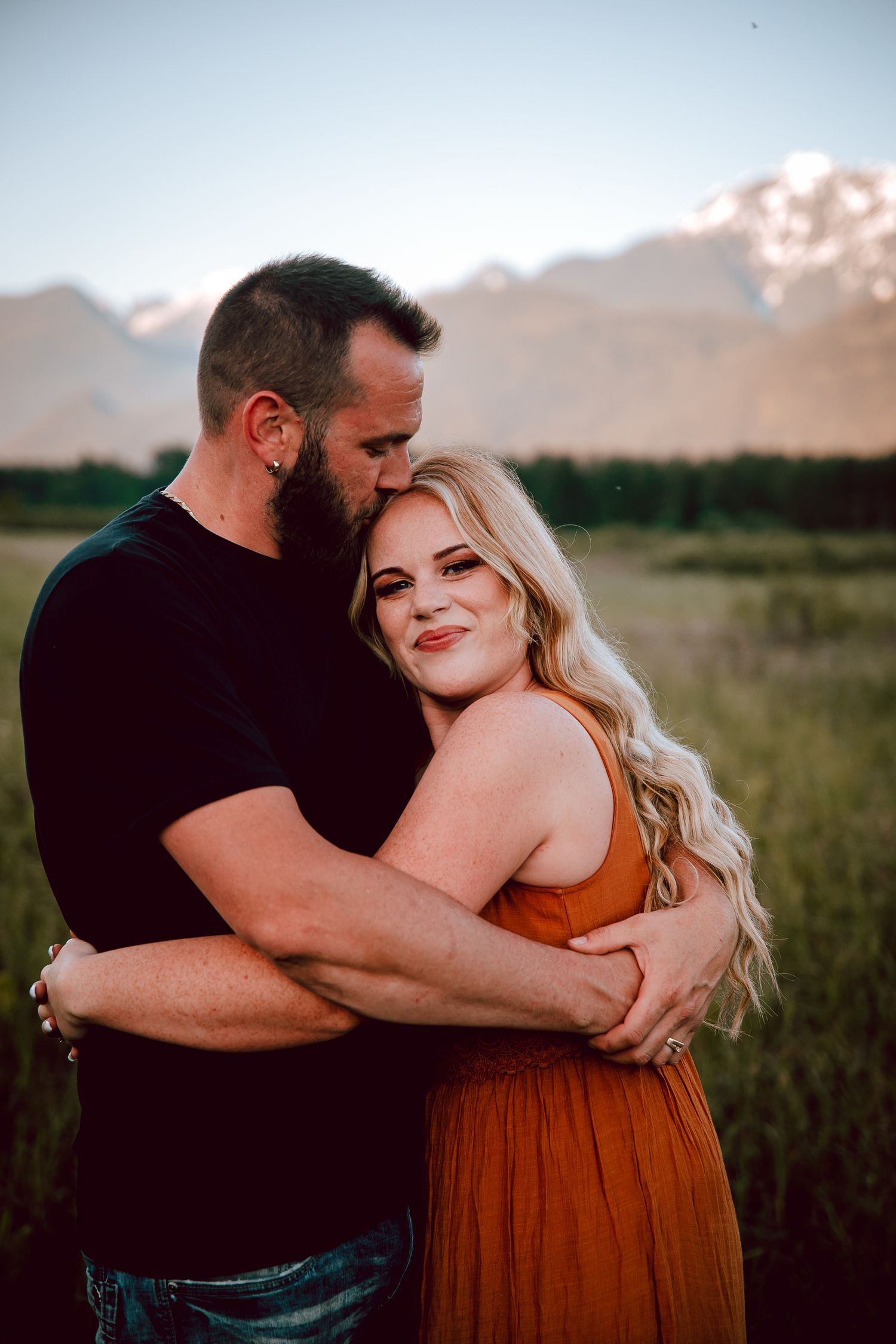 Intimate portrait of couple embracing in mountain field during sunset.