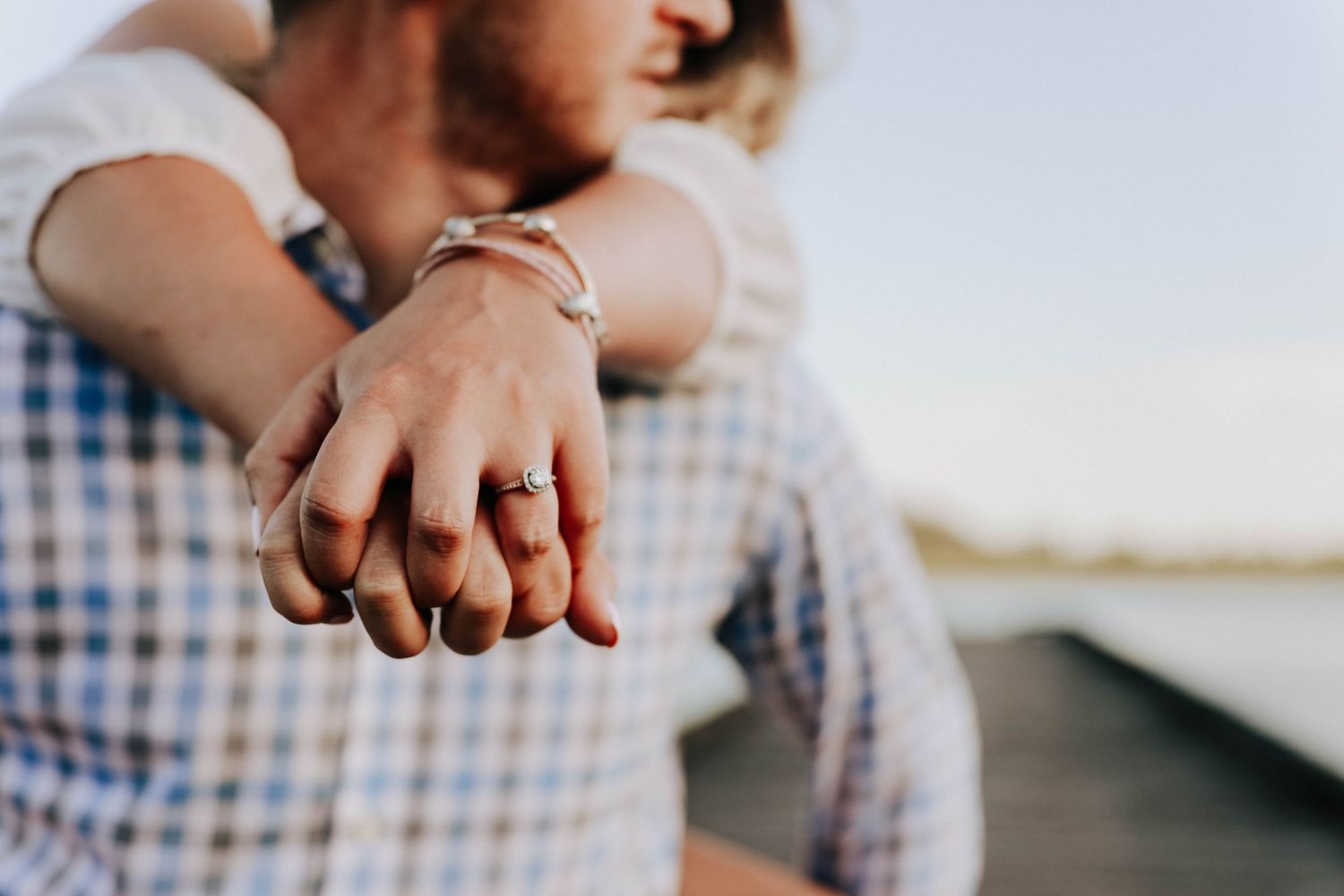 Close up of couple holding hands showing engagement ring on wooden dock.