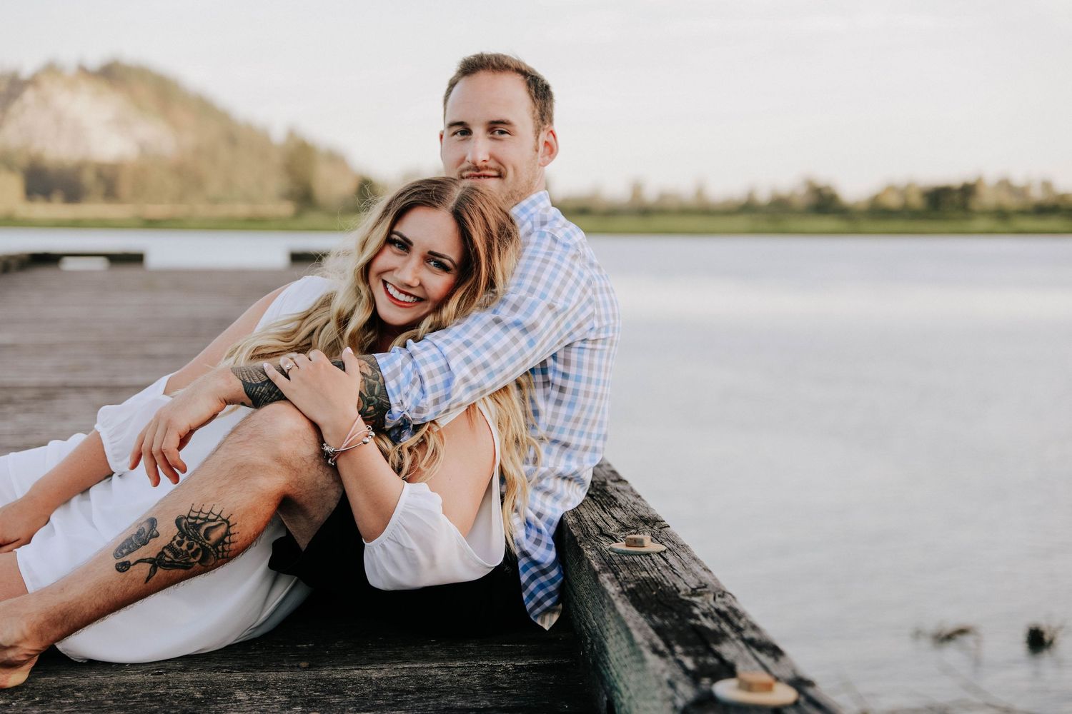 Playful couple laughing while sitting together on wooden dock by water.