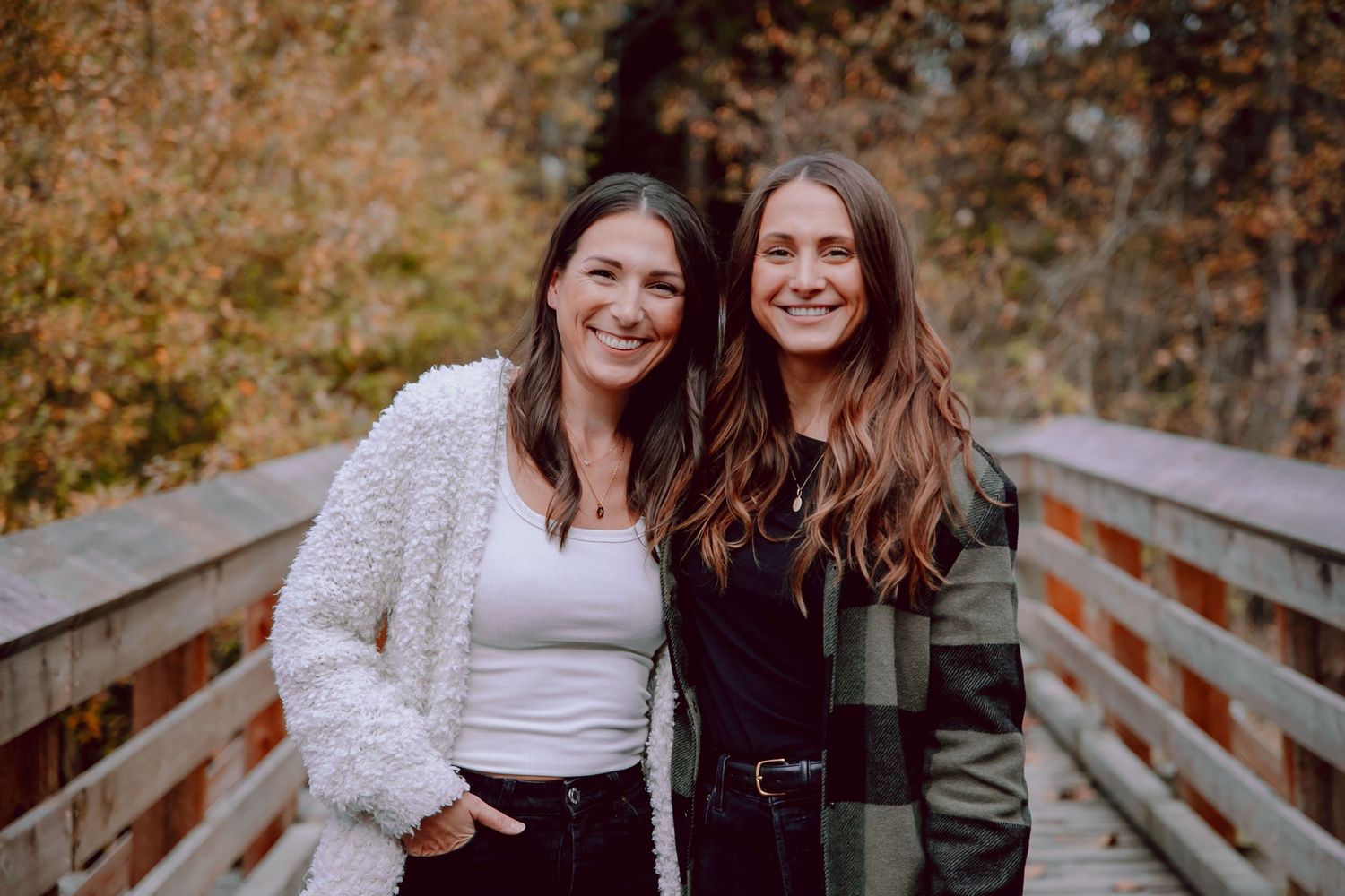 Two friends posing together on a wooden bridge during autumn with warm lighting.