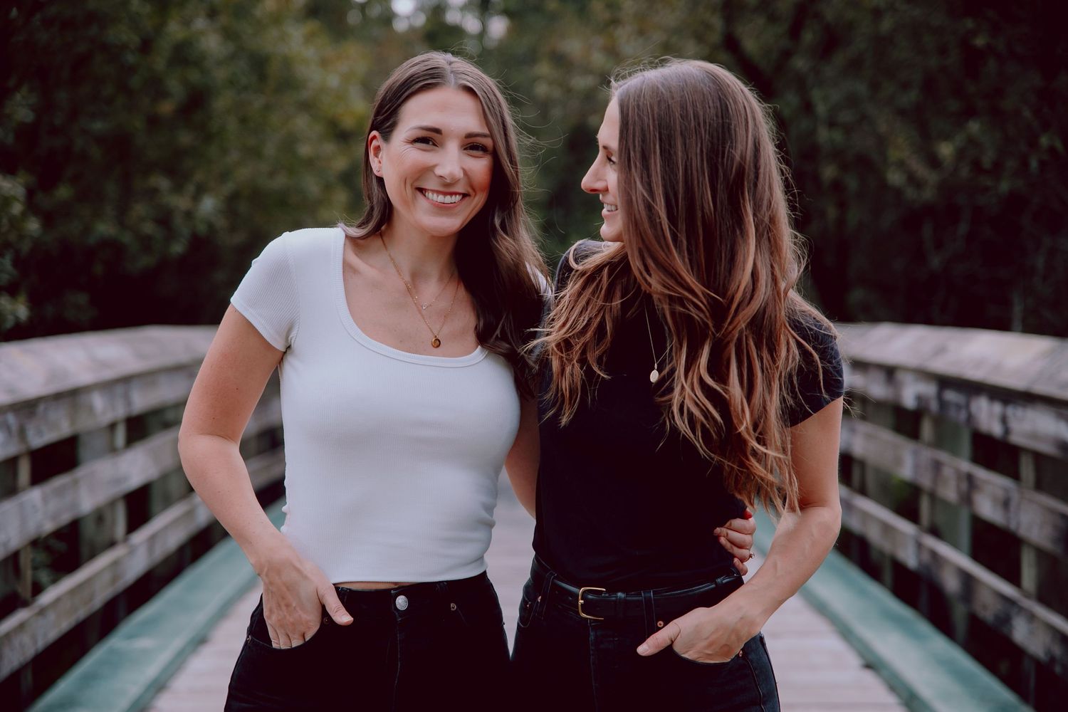 Two friends smiling and posing casually on a wooden bridge outdoors.
