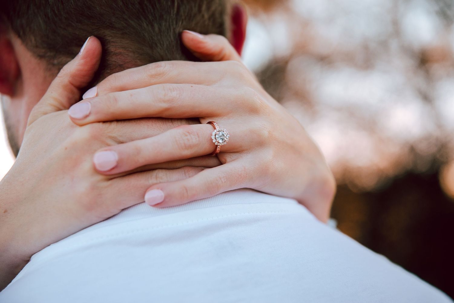 Close up of an engagement ring as hands embrace during a romantic moment.