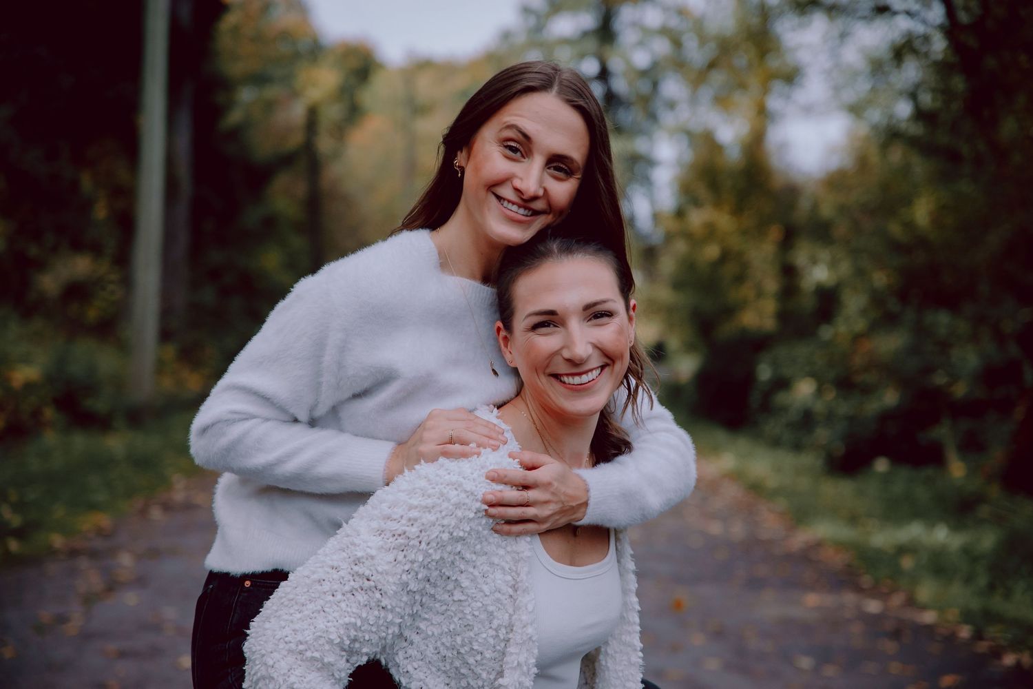 Two friends sharing a joyful embrace on an autumn path surrounded by trees.
