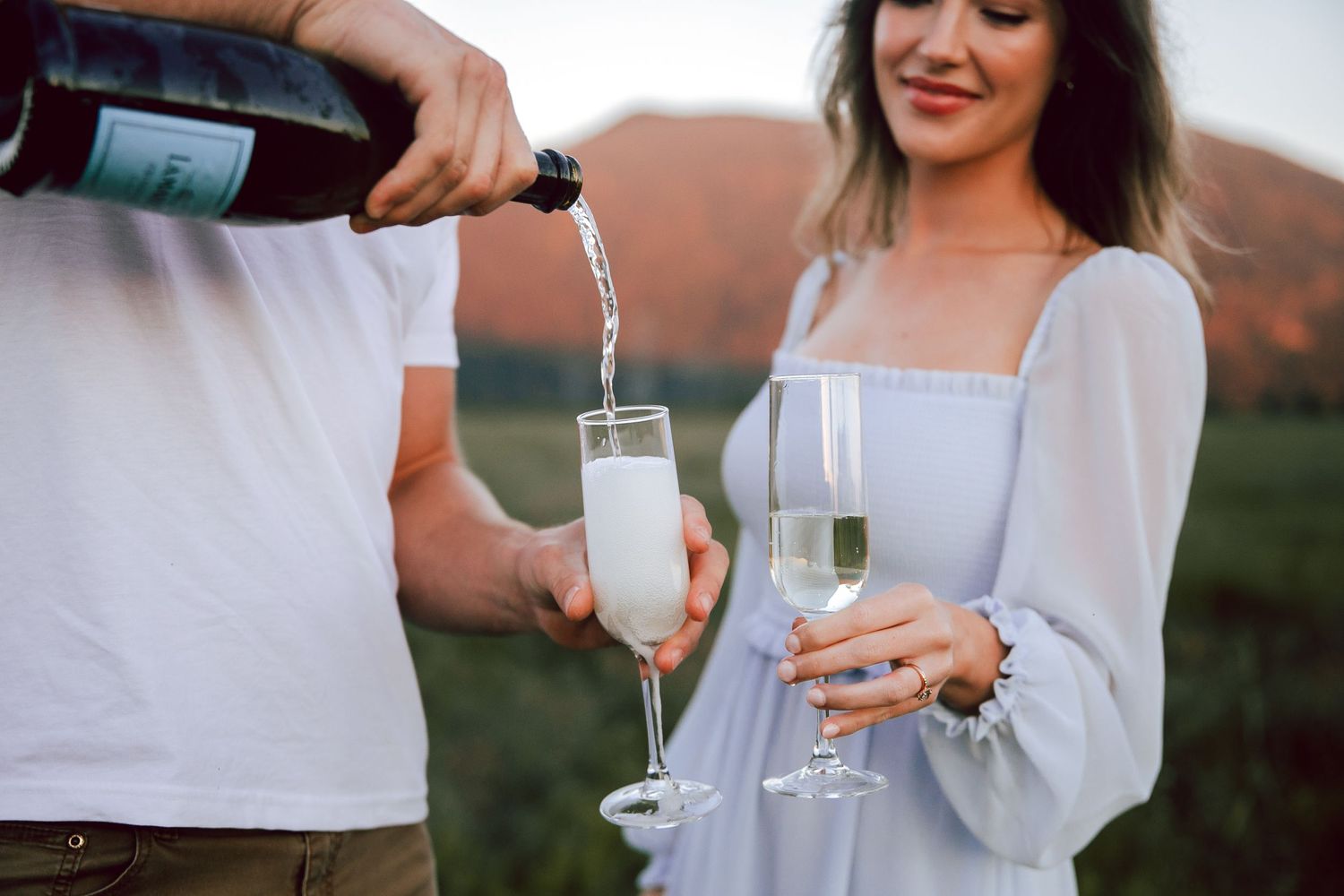 Couple pouring champagne into glasses during outdoor celebration.
