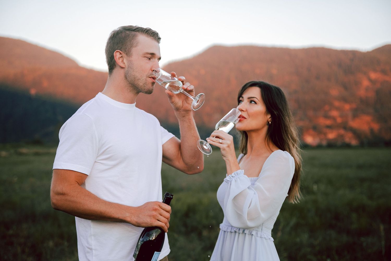 Couple enjoying wine together in a scenic mountain meadow at sunset.