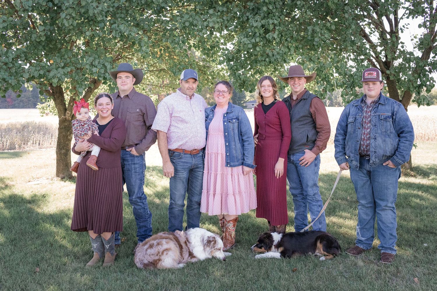Large family group poses together outdoors under green trees for a casual portrait.