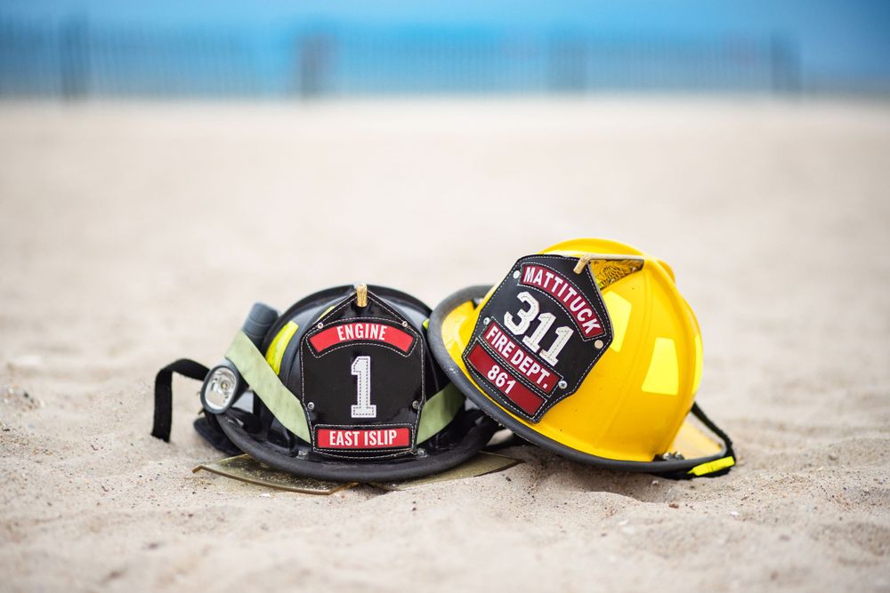 Two firefighter helmets, one black with red trim and one yellow, rest on a sandy beach.