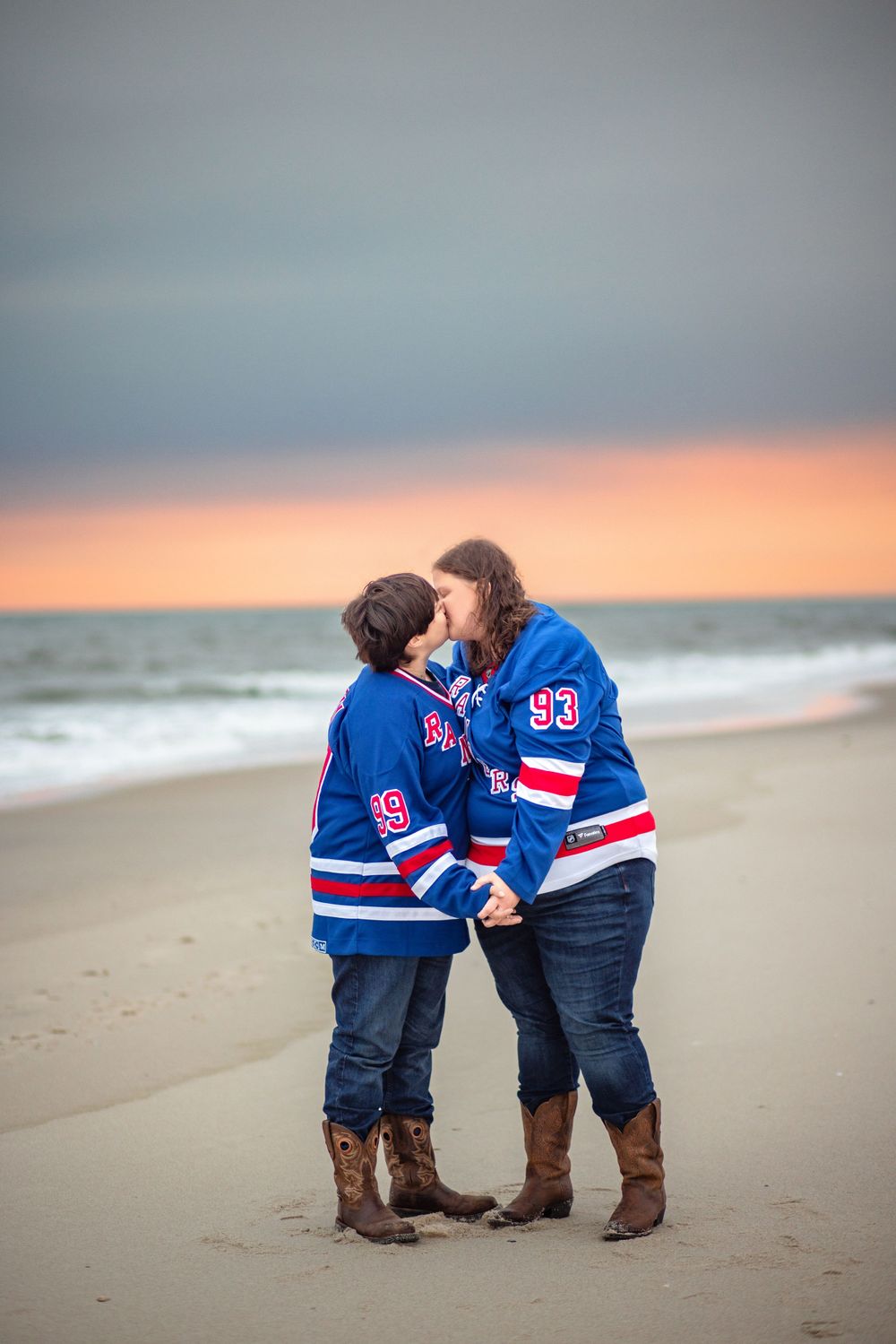 A couple in matching Rangers hockey jerseys share a romantic moment on the beach at sunset.