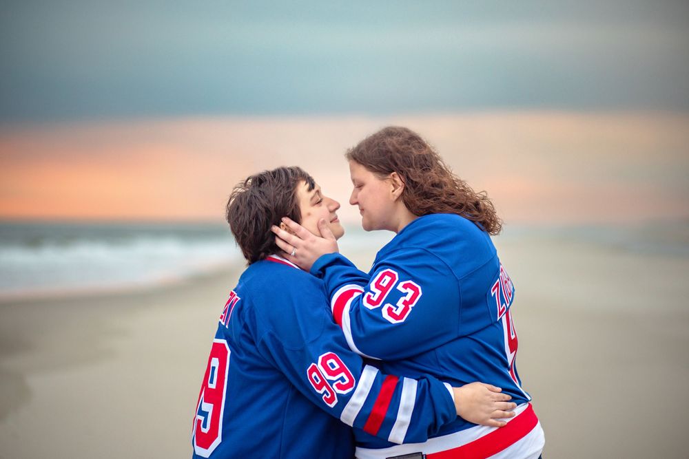 Two hockey fans in matching blue jerseys share a romantic moment at sunset on a beach.