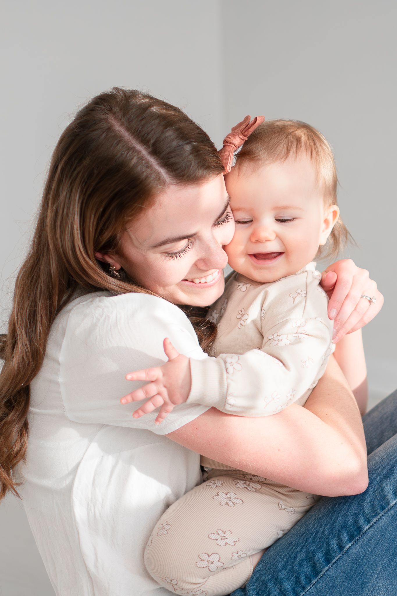 A joyful moment between parent and baby in white and beige outfits sharing laughter and cuddles.