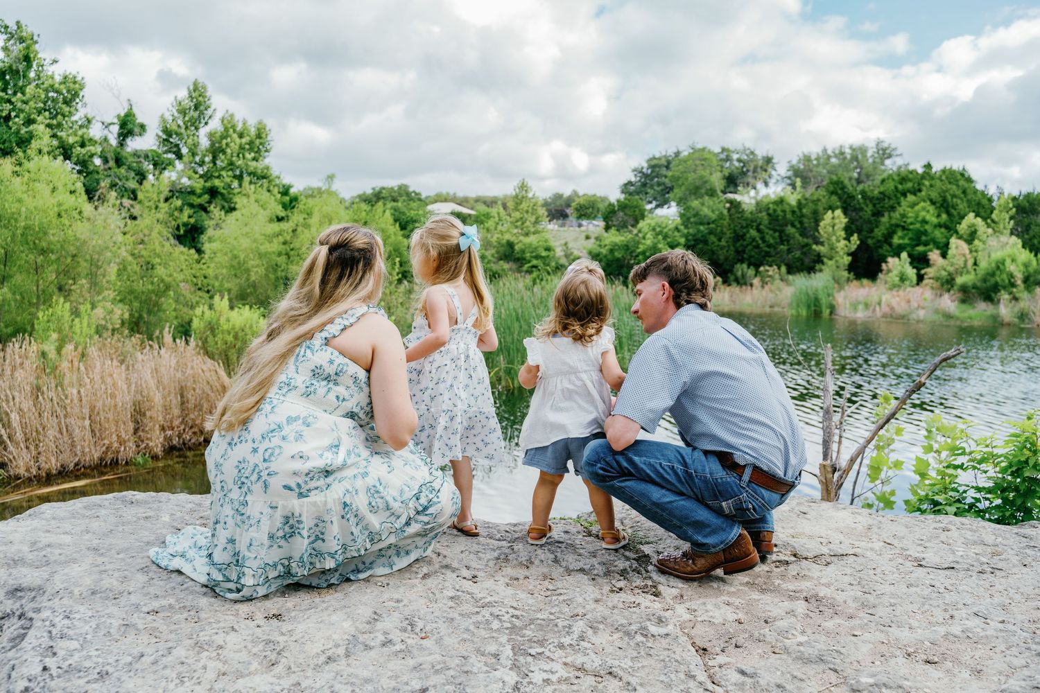 Family of four enjoying a serene lakeside view surrounded by lush greenery on a cloudy day.