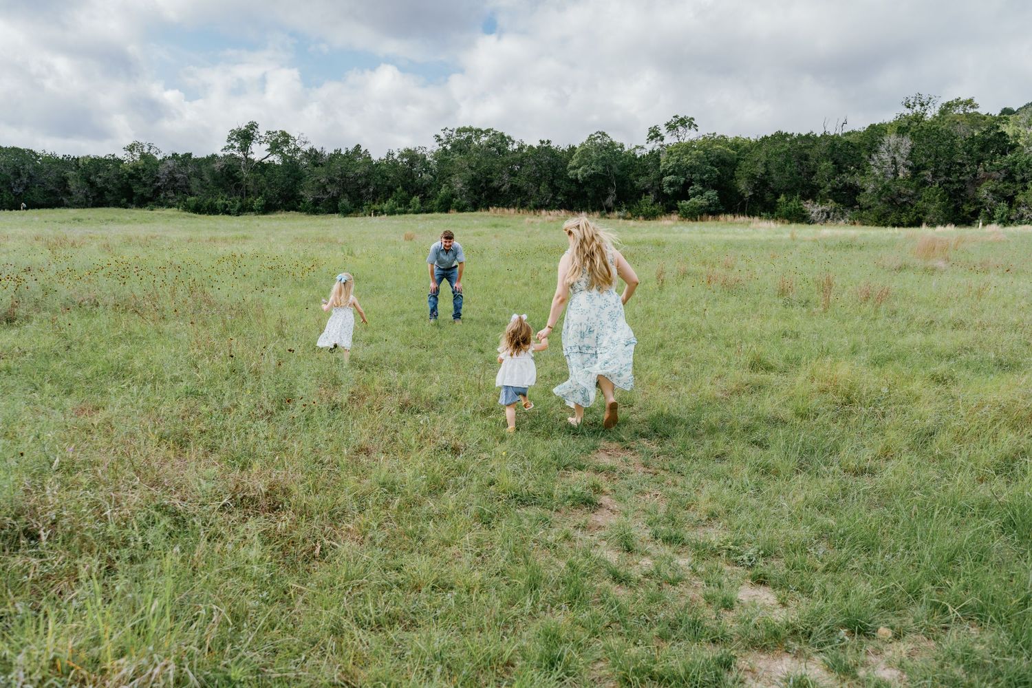 Children and a man running through a lush green meadow on a cloudy day in a wide open field.