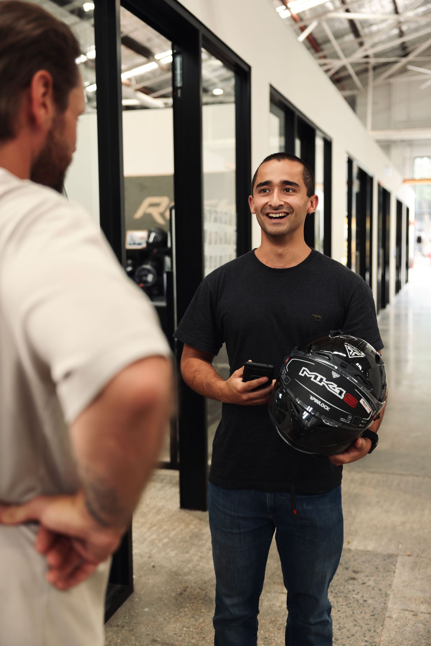 People interacting in an office hallway while holding motorcycle helmets.