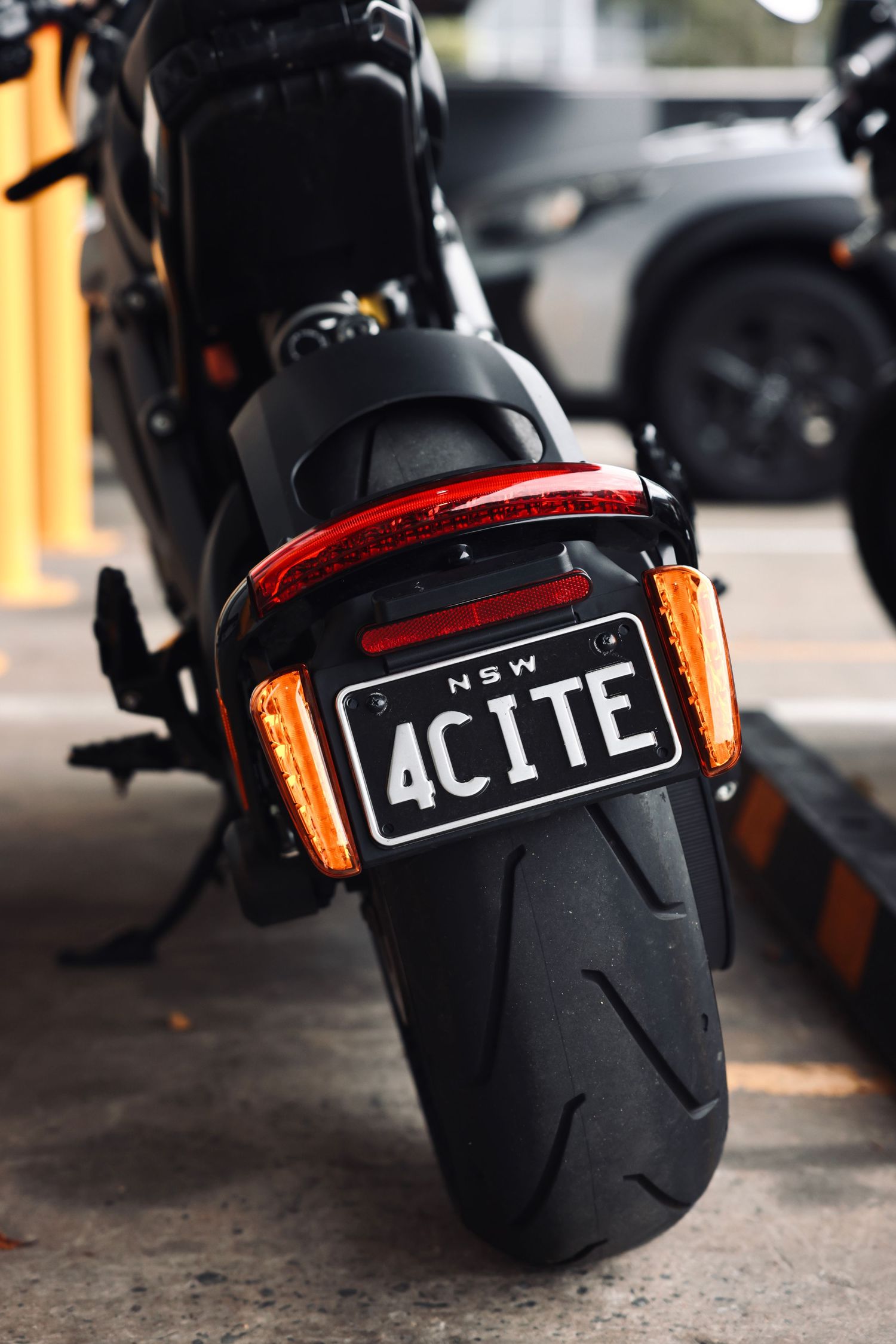 Close-up view of motorcycle license plates and tail lights with orange reflectors.