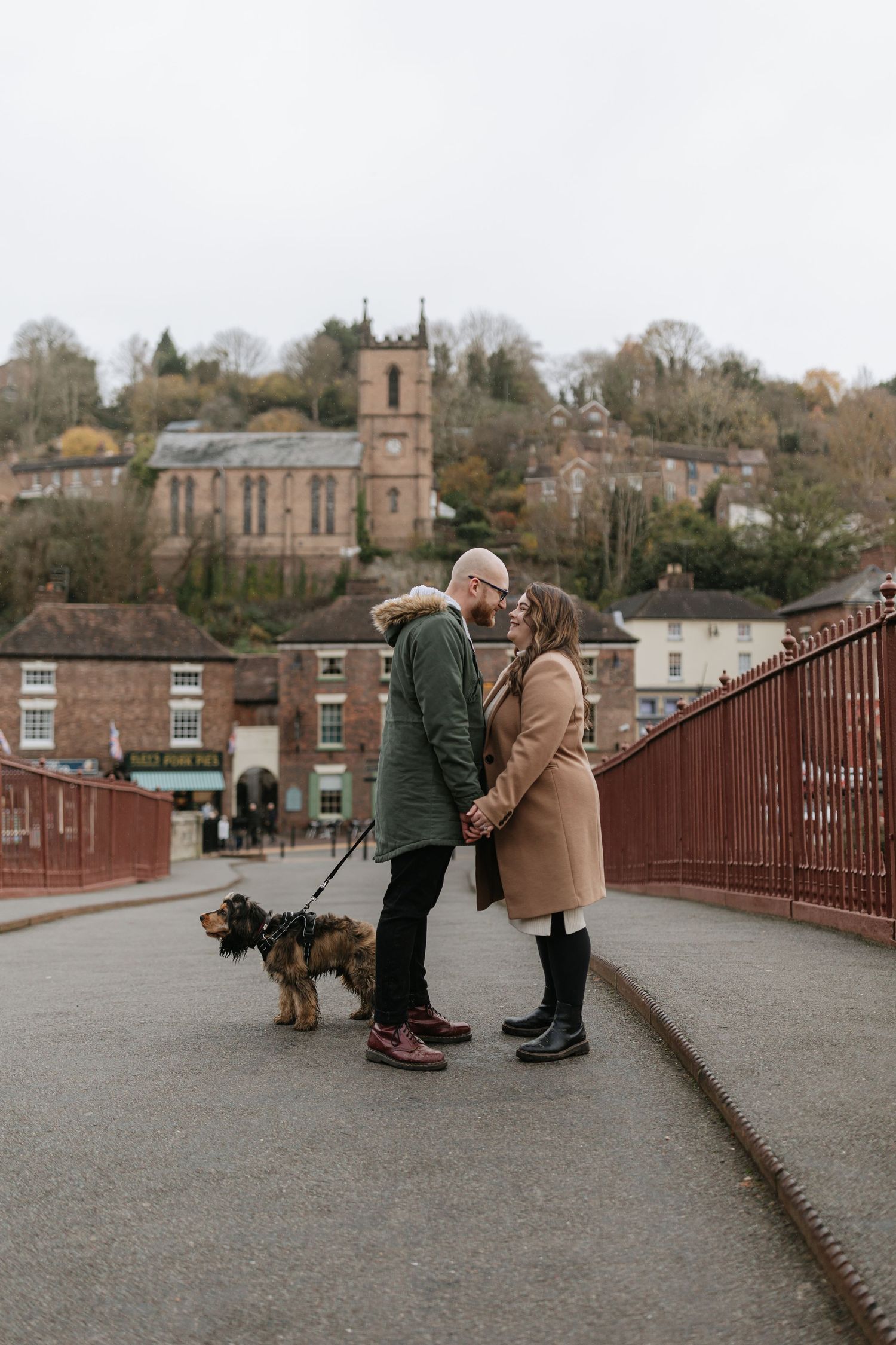 Three sequential photos show two people petting a large brown dog on a bridge with historic buildings in the background.