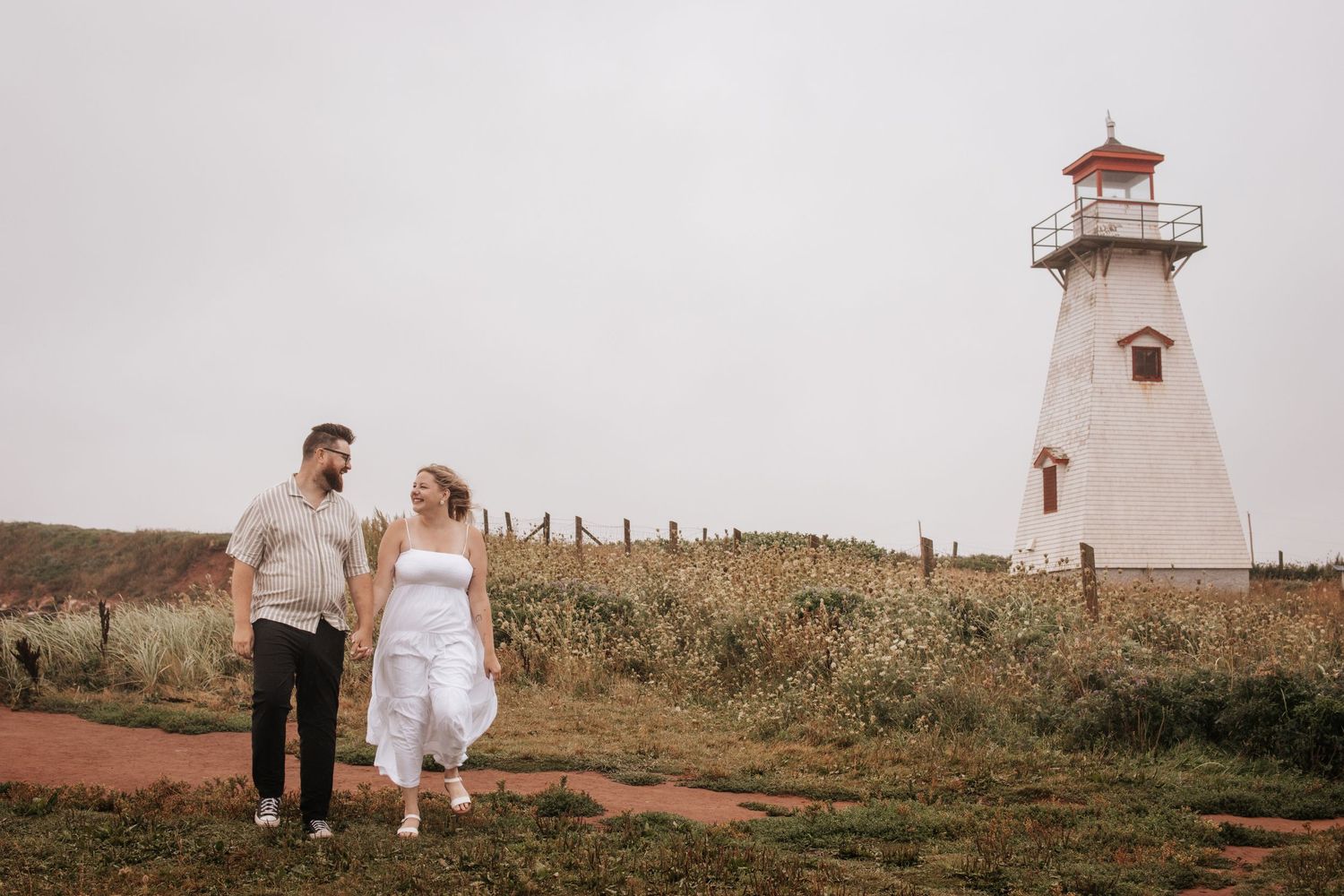 A rustic lighthouse stands tall against a cloudy sky on a grassy hill in Prince Edward Island.