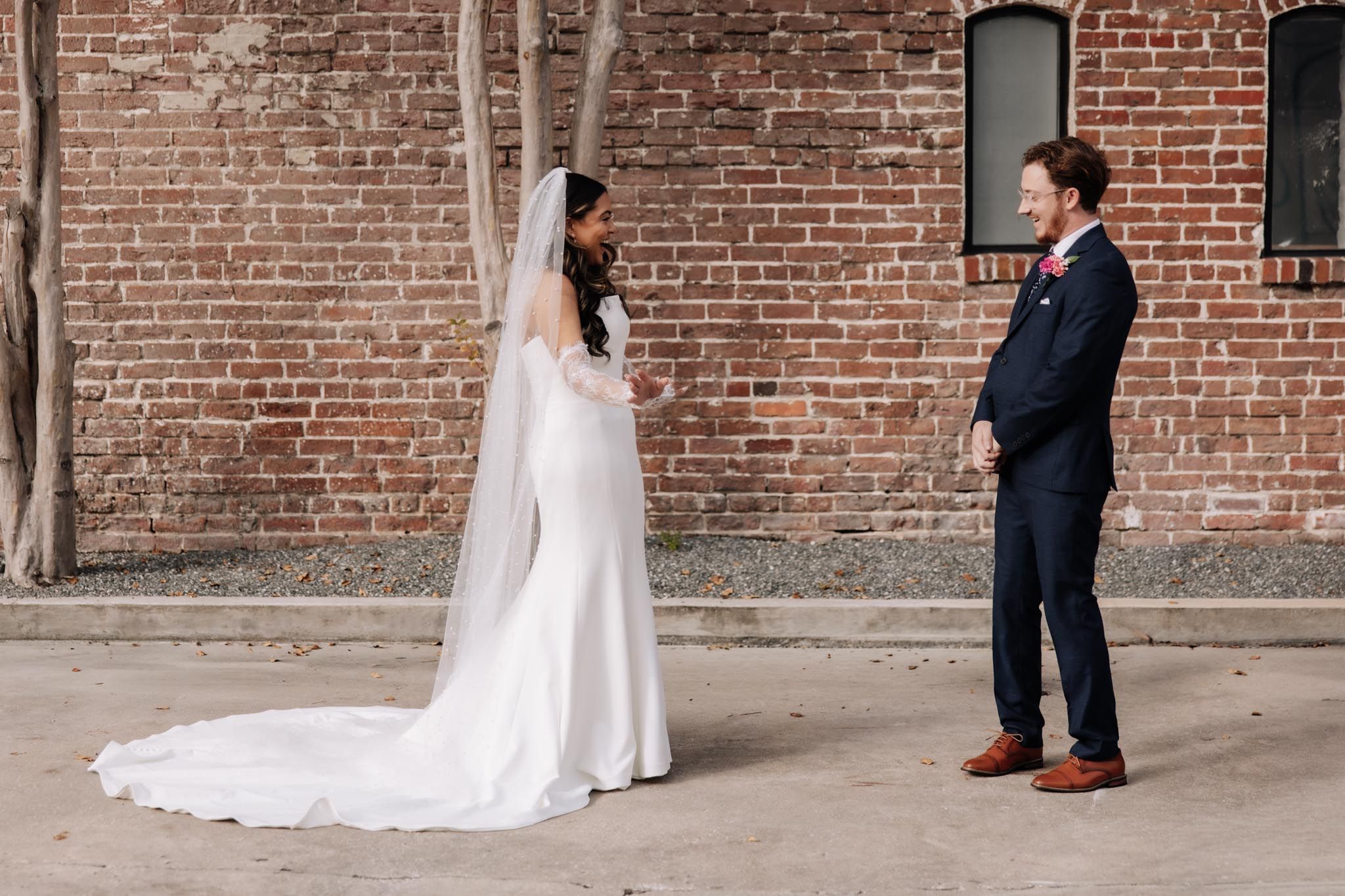 A wedding couple poses against a rustic brick wall in an urban setting.