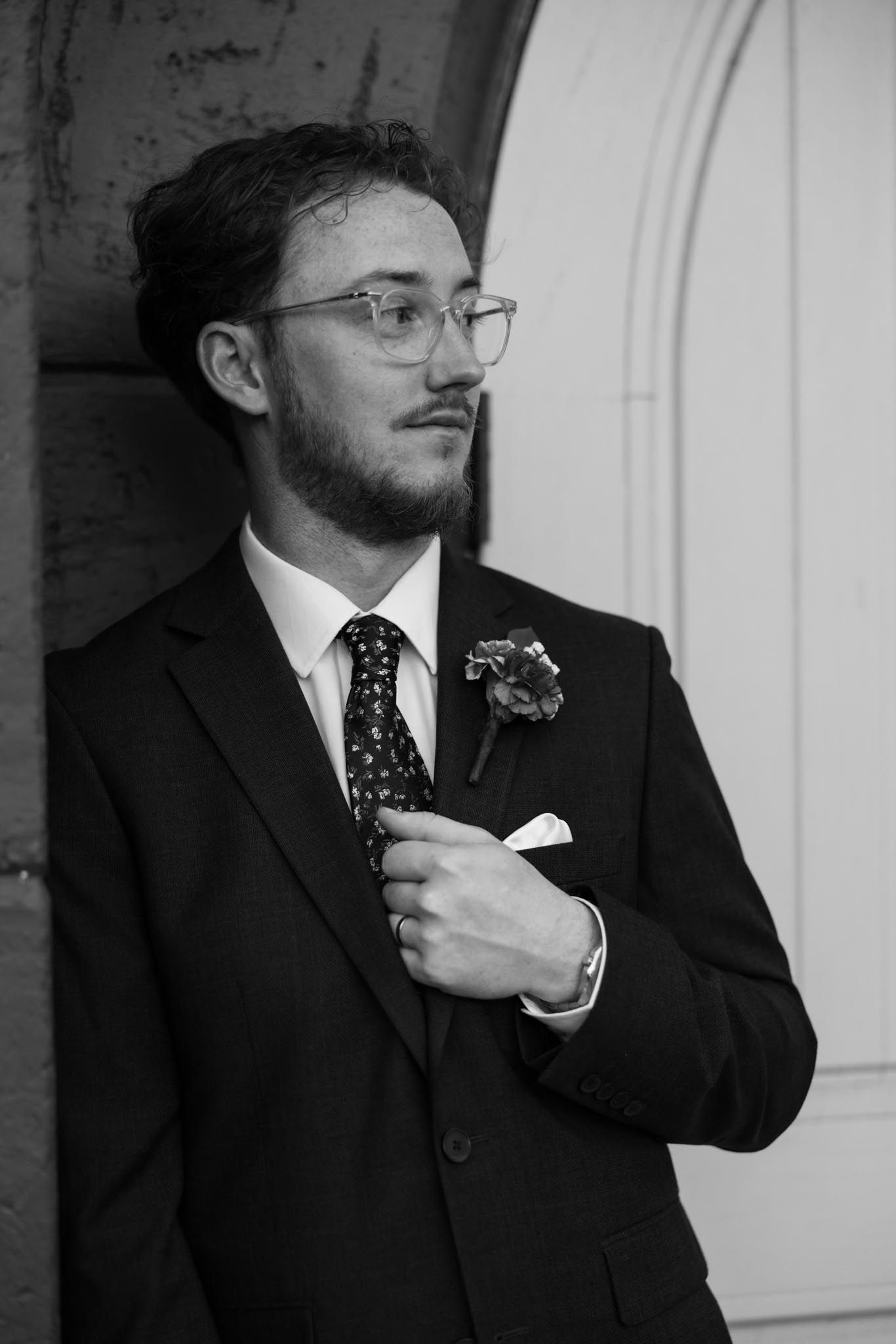 Black and white photo sequence showing a man in a suit and glasses adjusting his tie in four progressive shots.