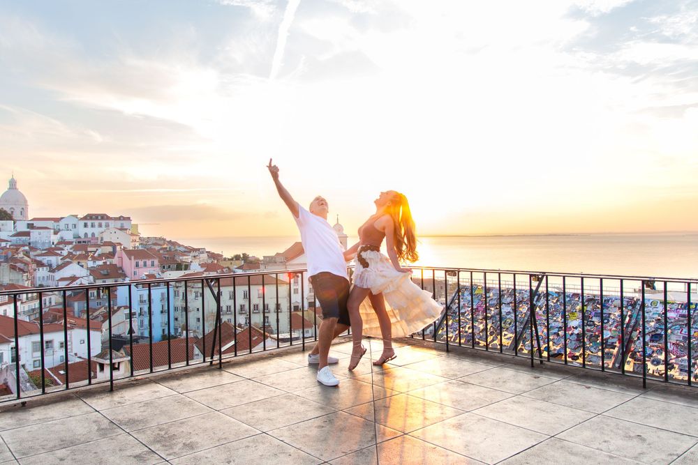 Silhouettes of people enjoying a colorful sunset at a scenic coastal overlook with railings.
