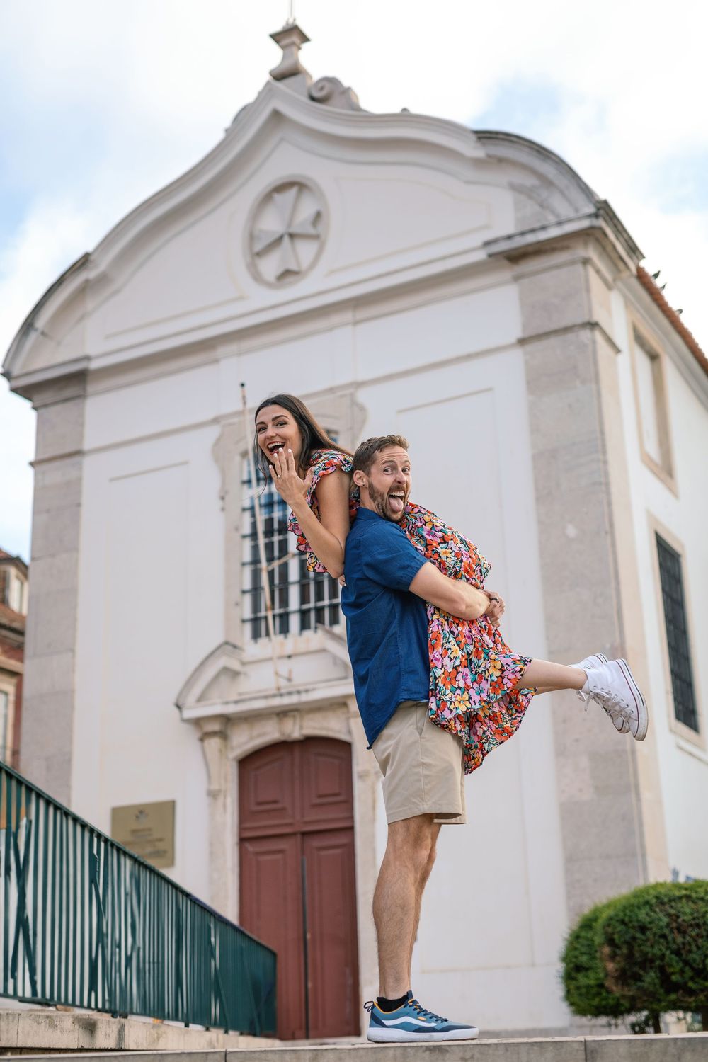 Playful couple enjoys a fun photo shoot in front of white colonial style buildings with ornate architecture.