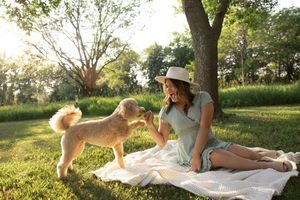 Sioux City, Iowa photographer. Young woman in hat sitting on blanket feeding a fluffy golden dog in sunny park.