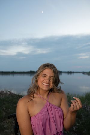 Sioux City, Iowa photographer. Smiling teenage girl in pink dress laughing near a lake at twilight with moon above.