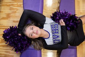 Sioux City, Iowa photographer. Cheerleader in black and white uniform lying on gym floor holding purple pompoms.