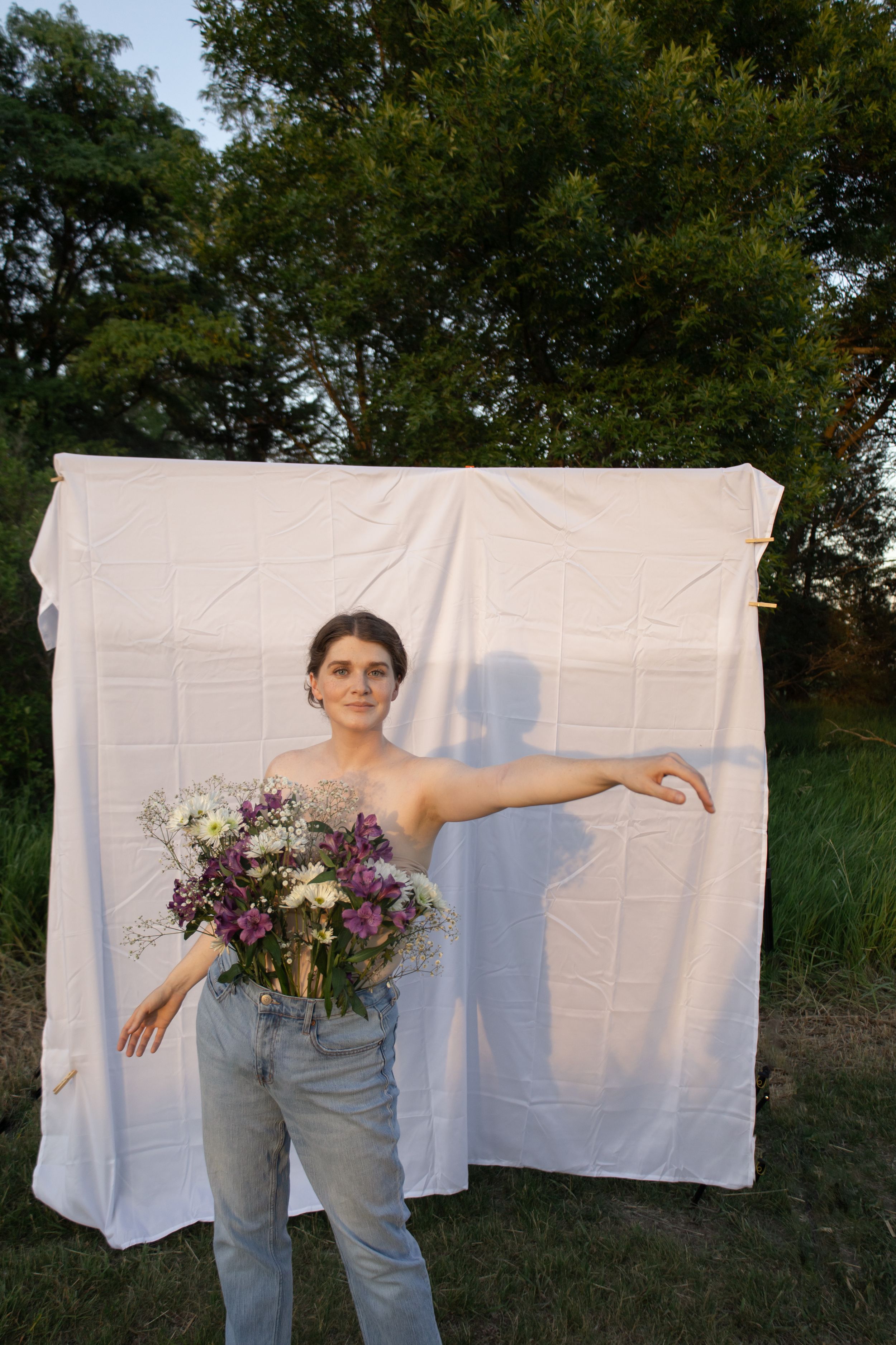 Sioux City, Iowa photographer. Young woman with short hair holds wildflower bouquet with arm extended before white sheet backdrop.