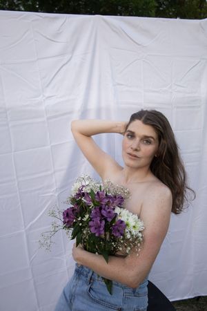 Sioux City, Iowa photographer. Brunette woman holds purple and white flower bouquet before white fabric backdrop outdoors.