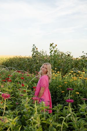 Sioux City, Iowa photographer. Blonde woman in pink dress standing among colorful wildflowers and sunflowers at golden hour.
